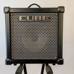 Černý kytarový kombozesilovač s kovovou mřížkou reproduktoru. V horní části mřížky je umístěn nápis CUBE. Nástroj má v rozích ochranné plastové rohy…