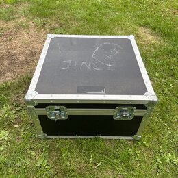 Černý transportní kufr s hliníkovými hranami a rohy. Na horní straně je bílým nápisem „JINC“ a vedle něj nečitelný symbol. Přední strana obsahuje dva…