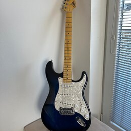 Elektrická kytara s tmavě modrým přechodovým lakem a bílým perleťovým pickguardem. Na hlavě hmatníku je viditelné logo Squier. Krk a hmatník jsou vyr…