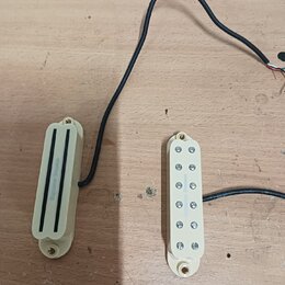 Dvě elektrické snímače v krémovém provedení s plastovými kryty. Levý snímač je typu humbucker s nápisem "Seymour Duncan". Pravý snímač je typu single…