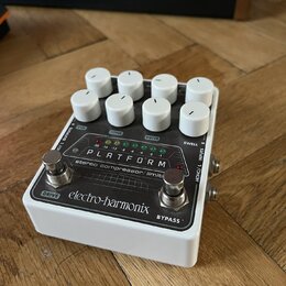 Bílý efekt pedál s osmi bílými oválnými ovladači. Na horním panelu je nápis PLATFORM a pod ním text stereo compressor/limiter. Ve spodní části je log…