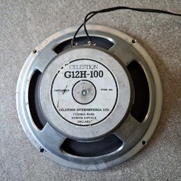 Fotografie zobrazuje reproduktor s kovovým rámem a černou membránou. Na zadním krytu je bílý štítek s nápisy CELESTION, G12H-100 a CELESTION INTERNAT…