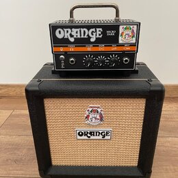 Černý kytarový kombozesilovač s béžovou texturovanou přední síťovkou a logem ORANGE. Na něm stojí malý černý zesilovač s nápisy ORANGE a MICRO DARK.…