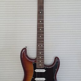 Elektrická kytara s trupem v hnědém sunburst provedení a černým pickguardem. Na hlavě hmatníku je viditelné logo "Squier". Nástroj má tři snímače typ…