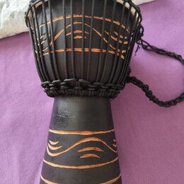 Černý djembe s bílou membránou, nataženou pomocí černých provázků. Tělo nástroje je zdobeno vyrytými vodorovnými a vlnitými liniemi, které odhalují h…