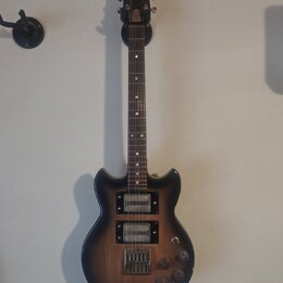 Elektrická kytara s tmavě hnědým gradientem (sunburst) a hnedým hmatníkem. Na hlavě je viditelné logo Epiphone. Nástroj má dva humbuckery, tři ovláda…