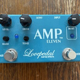 Modrý kytarový efekt s bílými nápisy AMP™ ELEVEN a Lovepedal CUSTOM EFFECTS. Na horní straně jsou tři černé otočné knoflíky s popisky LEVEL, DRIVE a…