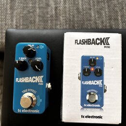 Modrý efekt pedál s nápisy FLASHBACK MINI a tc electronic. Na horní části jsou tři černé oválové knoflíky s popisky DELAY, F. BACK a LEVEL. Ve spodní…