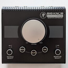 Černý monitor kontroler s velkým stříbrným volitkem uprostřed. Na horní části je nápis BIG KNOB PASSIVE MONITOR CONTROLLER a logo s postavou. Pod vol…
