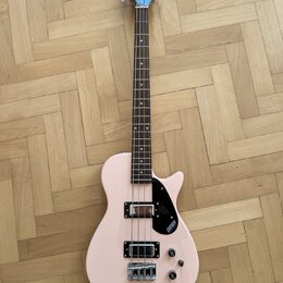 Světle růžová elektrická basová kytara s tmavým hnedým hmatníkem. Na hlavě nástroje je nápis GRETSCH a na černé plechovce u snímačů je rovněž logo GR…