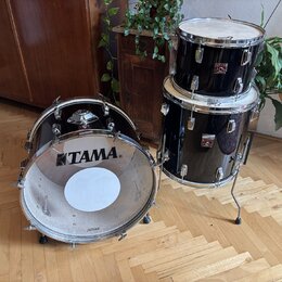 Černá bubnová sada tvořená basovým bubnem a dvěma tomami umístěnými na stojanu. Na přední коже basového bubnu je bílé logo TAMA. Na korusech tomů jso…