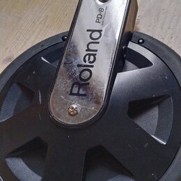 Elektronický činely značky Roland, model PD-8. Nástroj má černou gumovou plochu a kovový chromovaný držák s nápisem Roland PD-8. Na povrchu kovového…