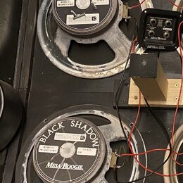 Dva reproduktory s černým papírem a šedými kovovými rámy, které vykazují známky opotřebení povrchu. Na obou jsou nápisy BLACK SHADOW, MESA BOOGIE a C…