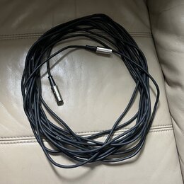 Černý kabel s kovovými konektory na obou koncích. Kabel je svinutý do kruhu a položený na světlém koženém povrchu. Na konektorech nejsou viditelné žá…