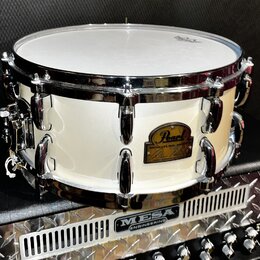 Bílá buben (snare) s chromovanými obručmi a ladicími šrouby. Na korpusu je zlatý oválný štít s nápisem Pearl a pod ním text SIGNATURE SERIES. Buben s…
