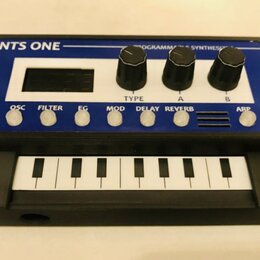 Černý kompaktní syntetizátor s modrým horním panelem a malou klaviaturou. Na horní části je bílý nápis NTS ONE a text PROGRAMMABLE SYNTHESIZER. Panel…