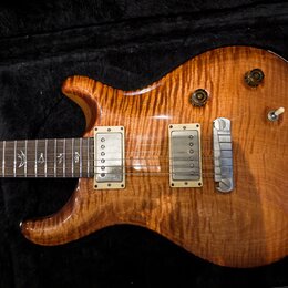 Elektrická kytara s tělem z plamenového javoru v medové barvě. Nástroj má dva humbuckery s krémovými rámečky, jeden bílý přepínač a dva černé oválné…