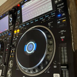 Černý digitální DJ player s displejem a velkým ovládacím jog-kolem. Na přístroji jsou viditelné nápisy Pioneer DJ a MULTI PLAYER CDJ-3000. Povrch je…