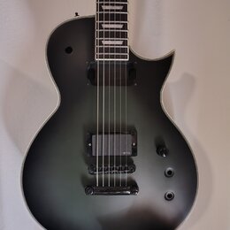 Kytara s matně černým povrchem těla a hnedým hmatníkem s bílými vložkami. Nástroj má dva humbuckery, přičemž na spodním je viditelné logo EMG. Na těl…