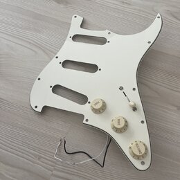 Bílá pickguard pro elektrickou kytaru s třemi výřezy pro snímače. Je na ní osazeno tři ovládací knofíky s nápisy TONE, TONE a VOLUME a jeden přepínač…