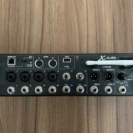 Černý digitální mixér s nápisy XAIR a XR12. Na pravé straně je bílé logo behringer v trojúhelníku. Zařízení obsahuje řadu vstupních konektorů, USB po…