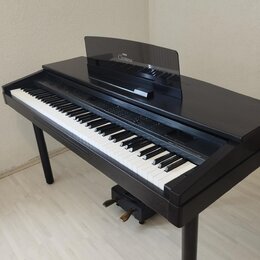 Černé digitální piano s klaviatura v klasickém provedení. Na hudebním stojanu je bílý nápis Clavinova a nad ním menší logo Yamaha. Nástroj je umístěn…
