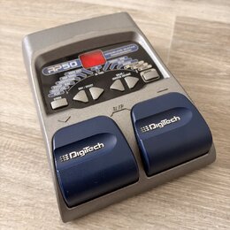 Šedý kytarový procesor s nápisem RP50 a MODELING GUITAR PROCESSOR. Zařízení má červený displej, řadu ovládacích tlačítek a dvě modrává pedály s bílým…