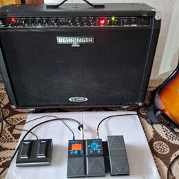 Černý kytarový kombozesilovač s nápisy BEHRINGER a V-TONE. Před zesilovačem jsou umístěny tři efektové pedály: černý pedál s nápisy EFFECT a SUSTAIN,…