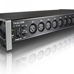 Černý rackový audio rozhraní s kovovými úchyty po stranách. Na přední straně je nápis TASCAM a model US-16x08, přepínače IN 1-4 a IN 5-8, kontrolka U…