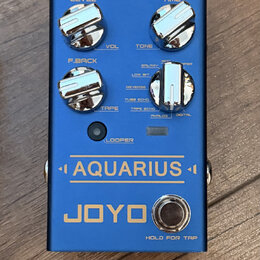 Modrý efekt pedál s nápisy AQUARIUS a JOYO. Na horní části jsou čtyři chromované ovládací knoflíky s popisky LEVEL, TIME, F.BACK a TAPE. U pravého kn…