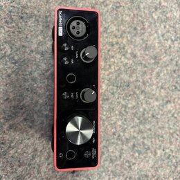 Červené audio rozhraní s nápisem Scarlett Solo. Na přední straně jsou dva otočné knoflíky GAIN, jeden velký knoflík MONITOR a tlačítka 48V, AIR, INST…