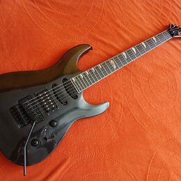 Černá elektrická kytara s tmavým hnedým hmatníkem a špičatou hlavou. Na hlavě je žlutý nápis KRAGLER. Nástroj má dva humbuckery, jeden jednosmykový s…