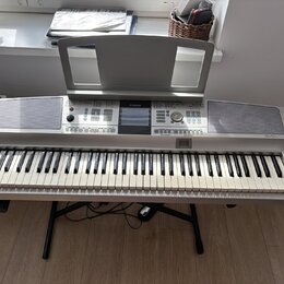 Stříbrný digitální klavír s černými a bílými klávesami, umístěný na černém X-stojanu. Na horním panelu je uprostřed logo YAMAHA a vpravo nápis Clavin…