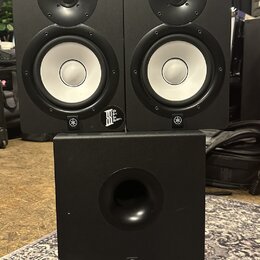 Sada tří černých studiových reproduktorů, dvě menší bedny umístěné nad jednou větší. Na spodní části každého reproduktoru je bílé logo Yamaha v kruhu…