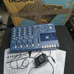 Modrý vícestopý magnetofon s nápisem TASCAM a označením PORTSTUDIO 414. Za přístrojem je umístěn originální karton s nápisy TASCAN, TASCAM a 4mkII. V…