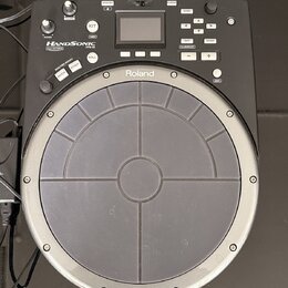 Černý elektronický perkusní pad značky Roland. Na zařízení je nápis HANDSONIC Expr/NATURAL a označení modelu HPD-20. Horní část obsahuje displej, ovl…
