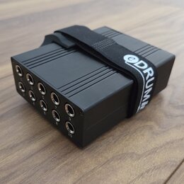 Černý obdélníkový box s žebrovaným horním povrchem a řadou deseti vstupních konektorů. Na boku jsou pod konektory viditelna čísla 1 až 10. Box je omo…
