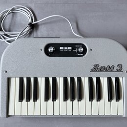Šedý elektronický klavír s bílými a černými klávesami. Na pravé straně je nápis Bass 3. V horní části se nachází ovládací panel s knoflíkem, přepínač…