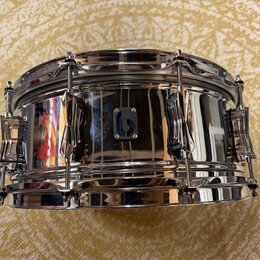 Stříbrný chromovaný snare drum s kovovým korpusem a chromovaným kováním. Uprostřed korpusu je umístěn malý čtvercový štítek s modrým nápisem SONOR. P…