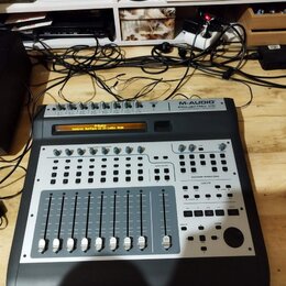 Černý kontrolér s kovovým horním panelem. V pravém horním rohu je nápis M-AUDIO PROJECTMIX I/O. Displej zobrazuje text M-Audio Control Surface is in…