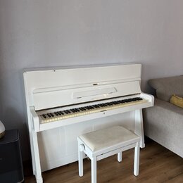 Bílé piano s doprovodnou bílou stoličkou s béžovým polstřením. Na přihradce nad klávesami je vidět nápis PETROF. Nástroj vykazuje mírné opotřebení v…