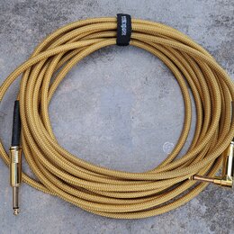 Zlatý pletený instrumentální kabel s konektory v zlatém provedení. Jeden konektor je rovný a druhý pravý. Na černém stahovacím pásku je bílý nápis ER…