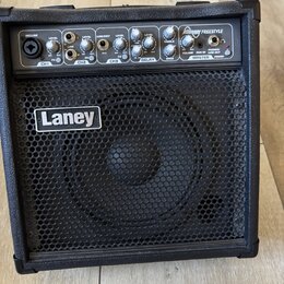 Černý kombo zesilovač s kovovou mřížkou reproduktoru, na které je bílé logo Laney. Horní ovládací panel obsahuje nápisy MIC/LINE, LEVEL, LINE/INST, D…