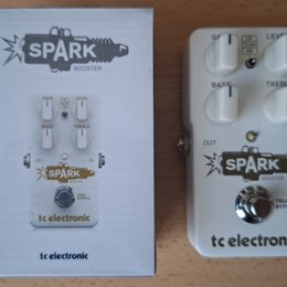 Bílá efekt pedál s nápisy SPARK BOOSTER a tc electronic. Pedál má čtyři bílé ovládací knoflíky s popisky GAIN, LEVEL, BASS a TREBLE, dále přepínač FA…