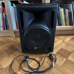 Černý kompaktní reproduktor s mřížkou a dvěma bočními rukojeťmi. Na spodní části mřížky je oranžové logo s nápisem soundnation. Před přístrojem leží…