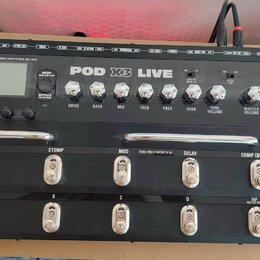 Černý kytarový procesor Line 6 POD X3 LIVE s kovovým pedálem vpravo. Na horním panelu jsou ovládací knofíky s nápisy DRIVE, BASS, MID, TREB, PRES, VE…
