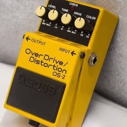 Žlutý efekt pedál s černým spínacím tlačítkem a nápisem BOSS. Na horní části jsou čtyři ovládací knoflíky s popisky LEVEL, TONE, DRIVE a COLOR a červ…