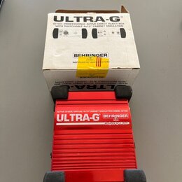 Červená DI box s hliníkovým žebrovaným povrchem a černými gumovými nohami. Na zařízení je bílý nápis ULTRA-G, logo BEHRINGER a text ACTIVE DI-BOX/VIR…