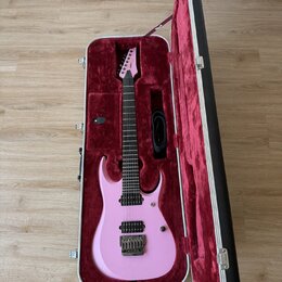 Růžová elektrická kytara v tvrdém kufru s červeným polstrováním. Na hlavě hmatníku je bílý nápis Ibanez. Kytara má dva humbuckery, Tremolo most a čer…