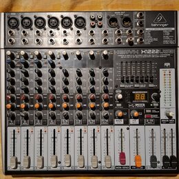 Stříbro-šedý mixážní pult značky behringer s nápisem XENYX X1222USB. Zařízení obsahuje 6 mikrofonních vstupů, několik linkových vstupů a faderové ovl…